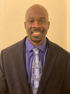 Clausell Mathis smiles. He is wearing a suit and tie and a purple dress shirt