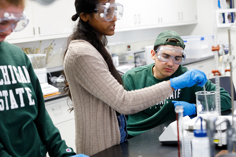 three students with safety glasses work in a chemistry lab