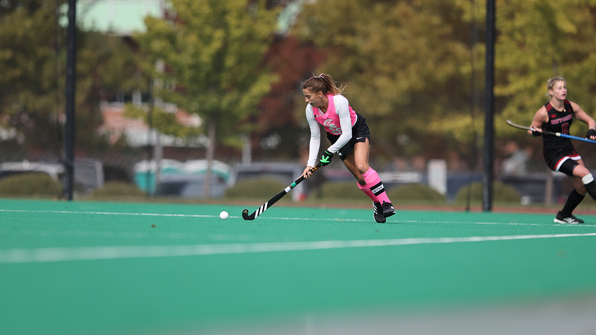 Ashley Harlock with a pink Spartan uniform on, hits the ball on the turf with a competitor in the background