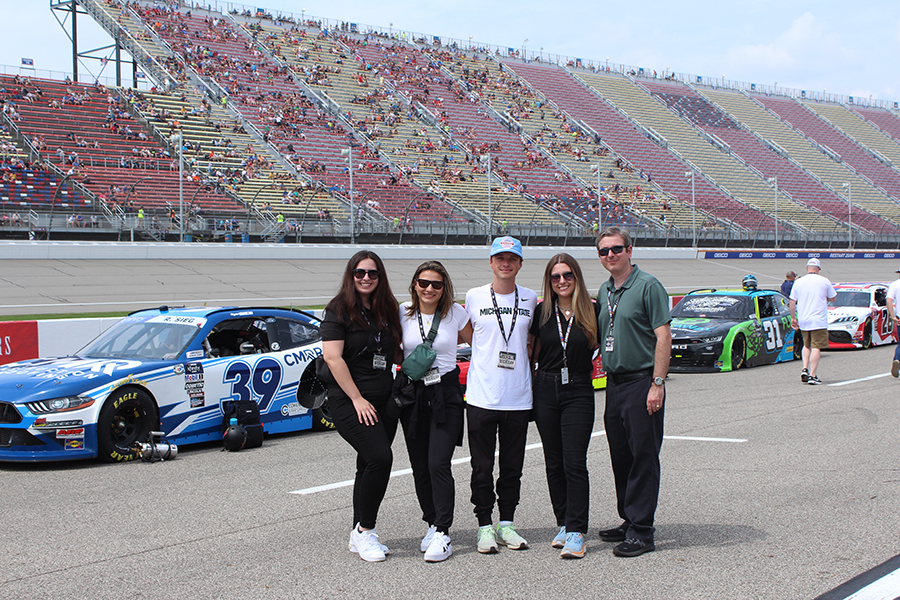 The research team stands on pit road with Nascars behind them