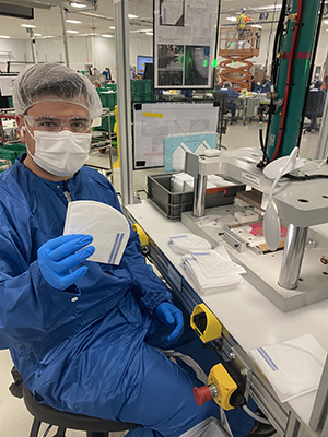 Brendan Wiley, in protective gear, holds up a mask in the GM plant in which he worked this summer