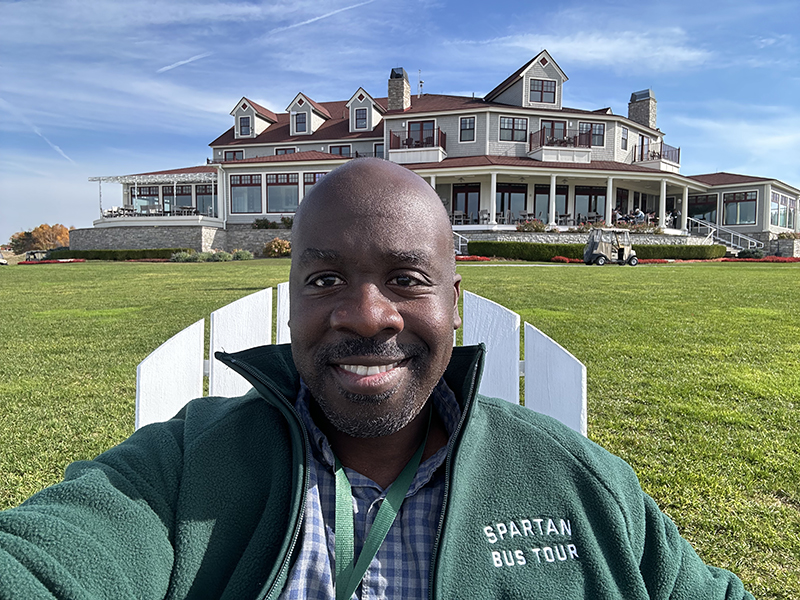 Arcadia Bluffs golf course on Lake Michigan in the background. Mathis sits in an Adirondack chair in the foreground