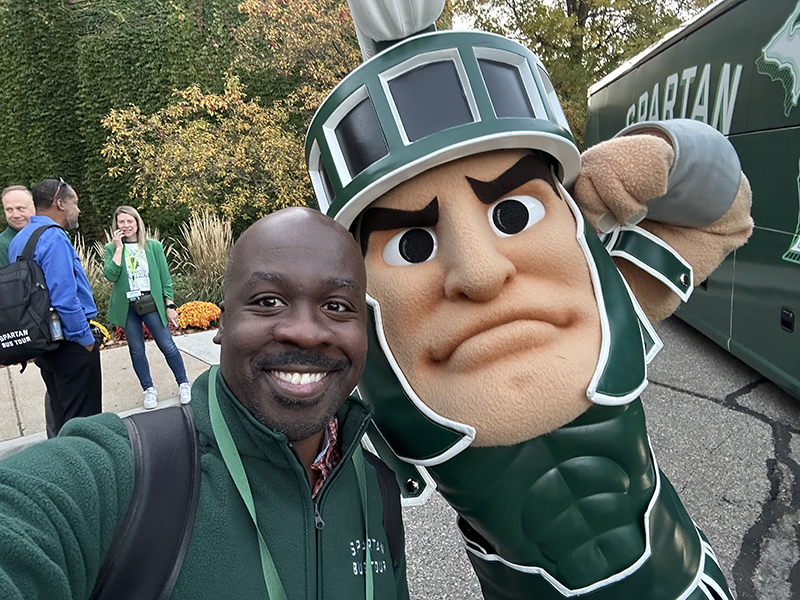 Clausell Mathis poses with Sparty, the MSU Mascot, outside of the bus from the Spartan Bus Tour