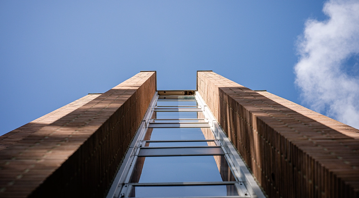 view skyward from the base of one of the Holmes Hall residence hall towers. Sky is blue, glass reflects sun and shadows, and contrasts with orange brick