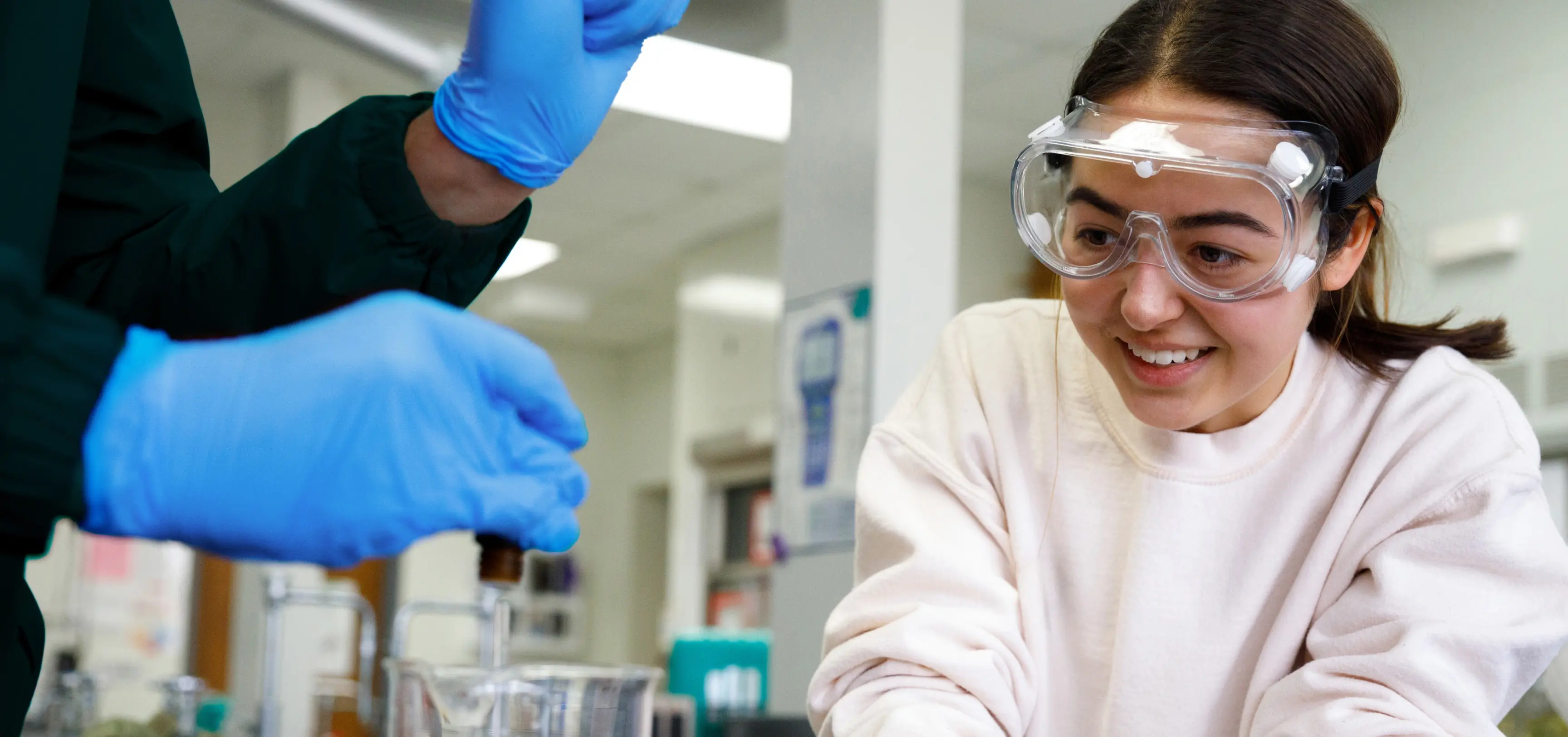 Student smiling and wearing safety glasses working in a lab