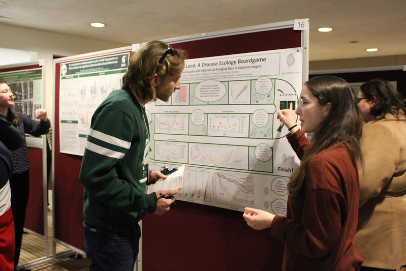 A student presents a research poster to an evaluator at the 2025 Research Showcase
