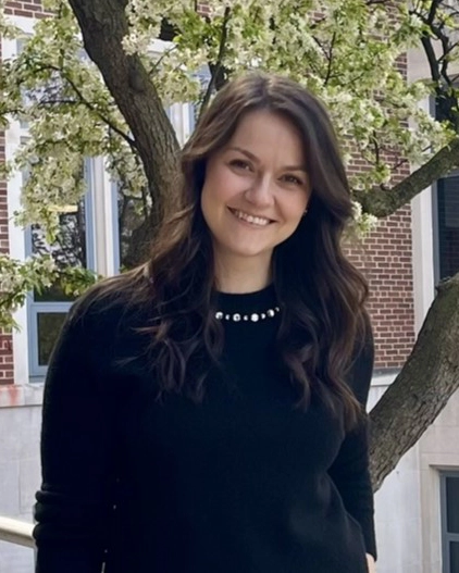 Ani Hristova has long dark brown hair and is smiling, wearing a black top, black jacket, and a necklace