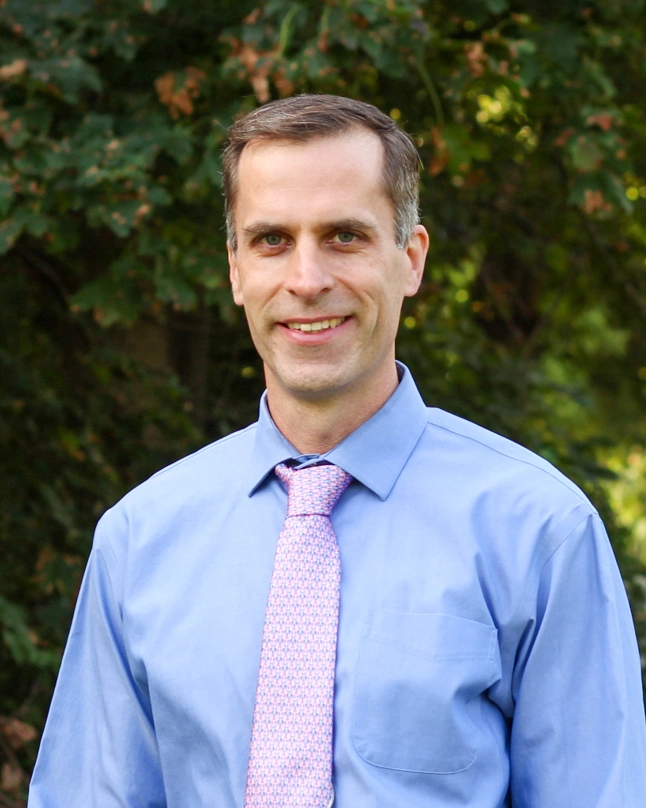 Ryan Sweeder wears a blue dress shirt and pale pink tie. He has dark hair