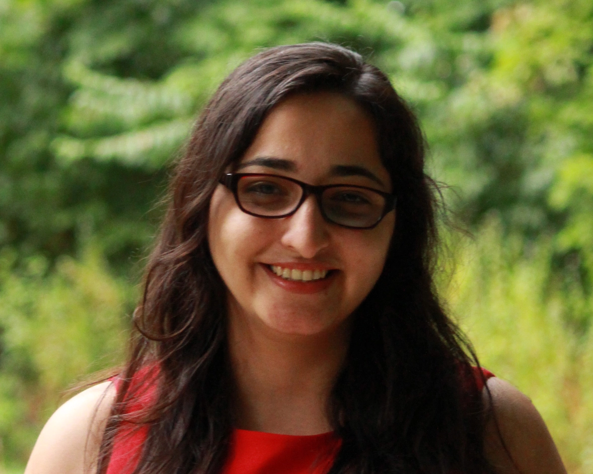 Shahnaz Masani wears a red sleeveless dress. She has long, dark hair and glasses