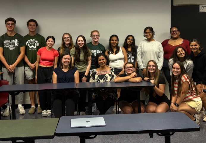 15 students and two administrators smile in one of the Holmes Hall classrooms