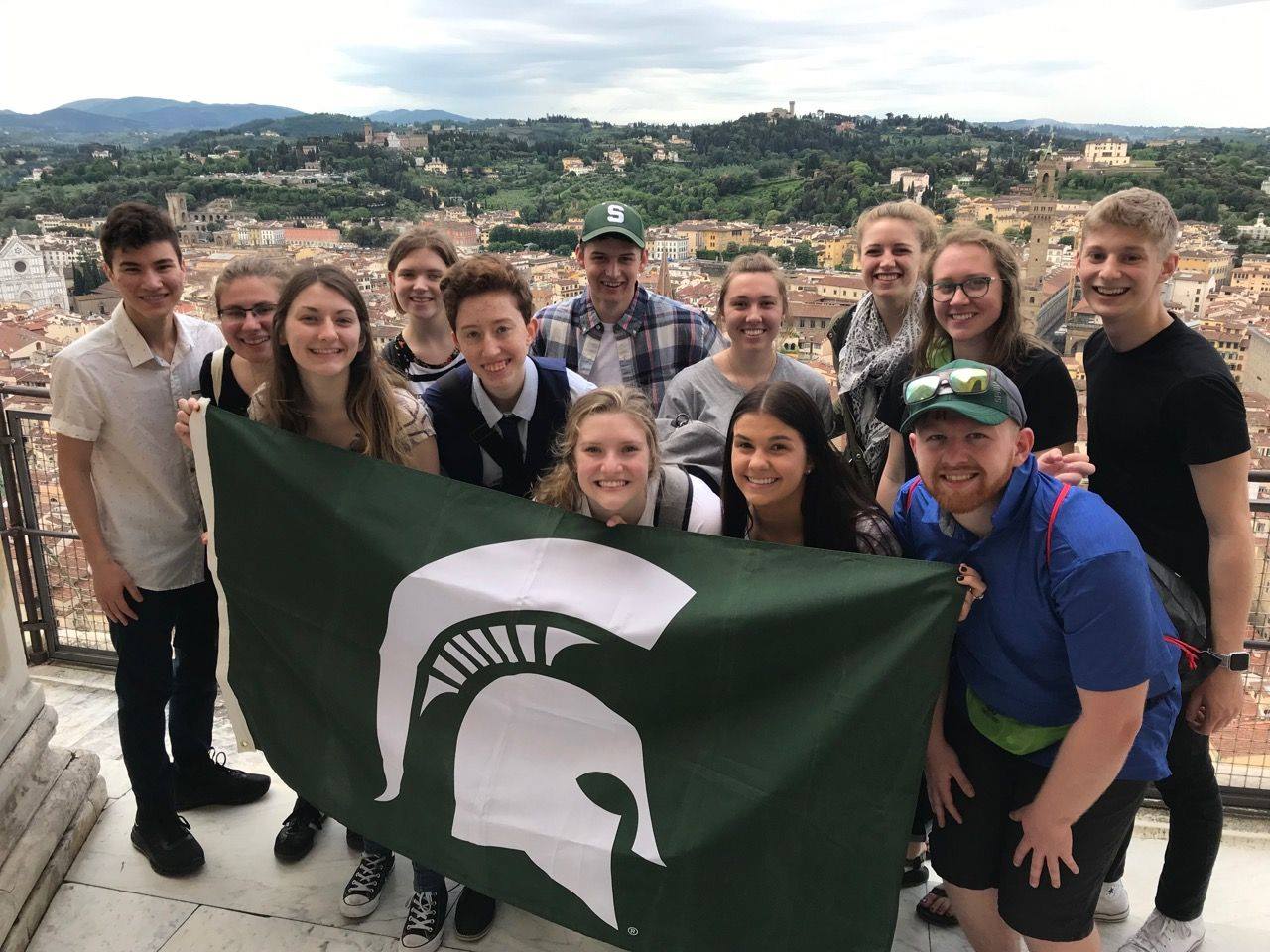 students smile and hold a Spartan flag on the roof of a building in Florence, Italy