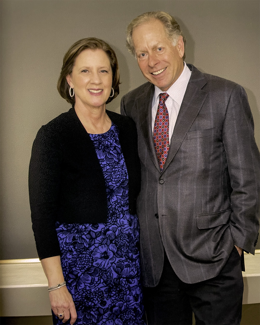 Nancy McLelland and Mike McLelland. Nancy has chin-length brown hair and wears hoop earrings, a blue floral dress and a black jacket. Mike wears a gray suit with a subtle pattern, a white dress shirt and a red tie with a blue and gold pattern.