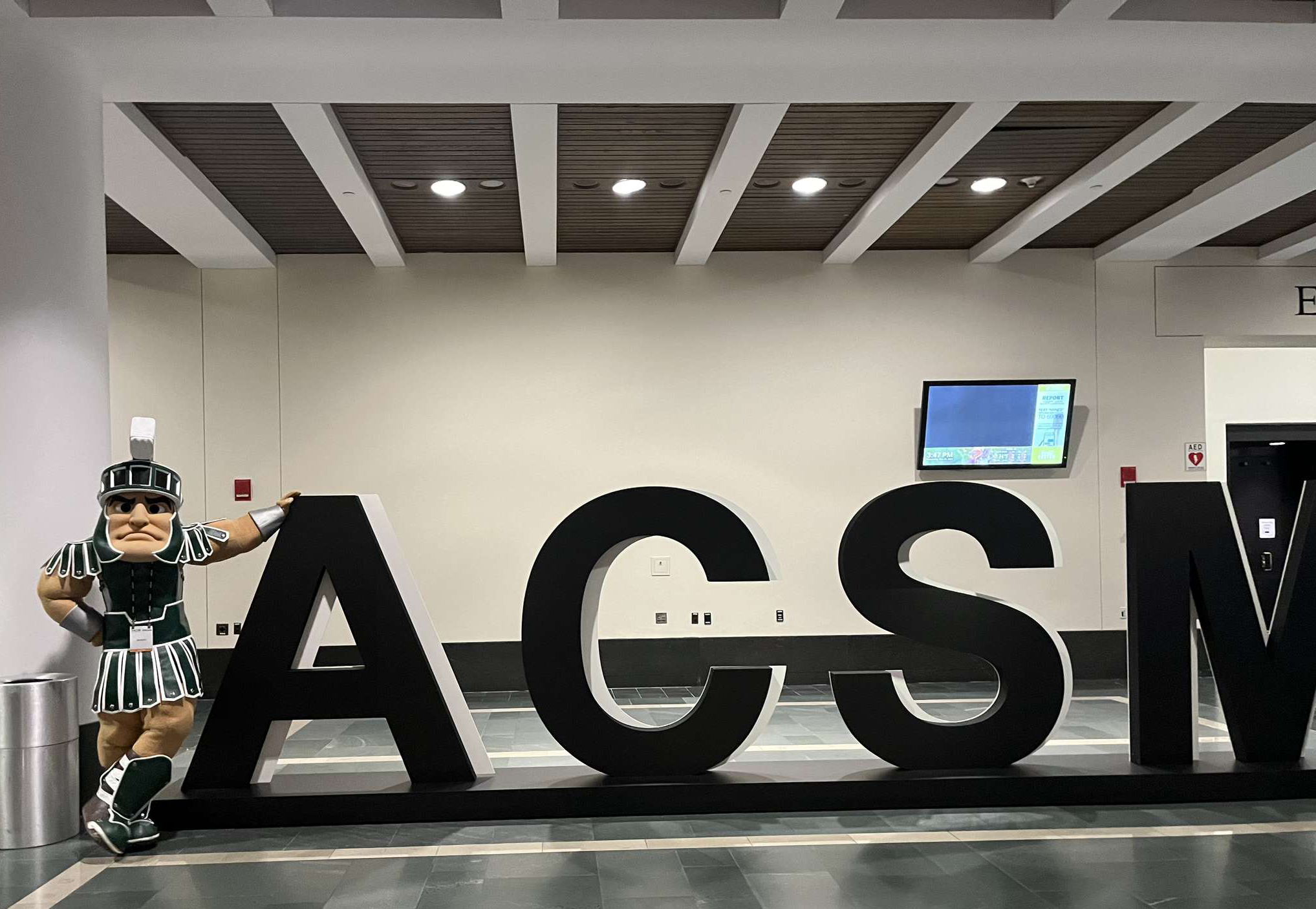 Morrison, in Sparty uniform, leans against the architectural sign for the American College of Sports Medicine