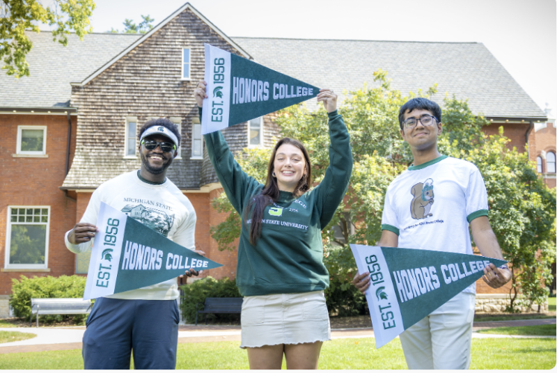 students hold honors college pennants in front of Eustace-Cole Hall, home of the MSU Honors College