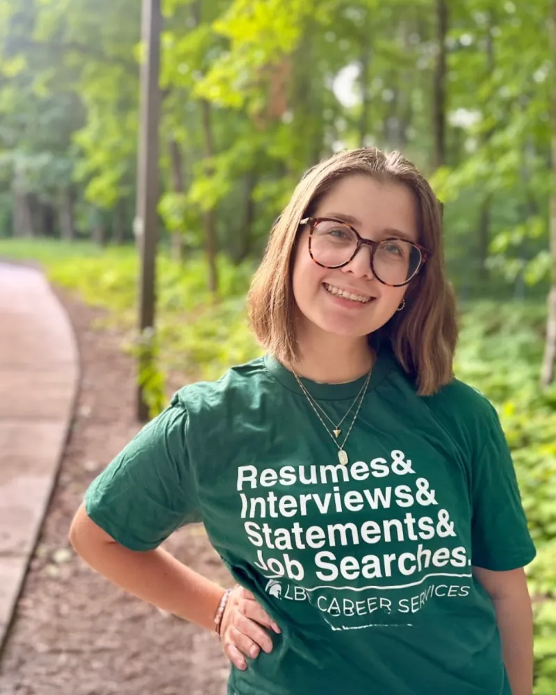 Mary Defrees smiles. She has short brown hair, glasses, and an LBC shirt that says Resumes, Interviews, Statements & Job Searches--services of the LBC Career Team