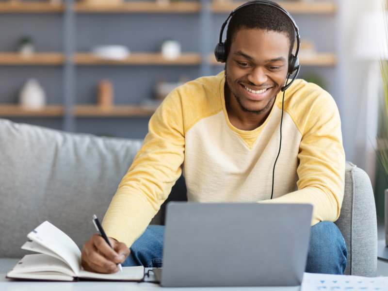 student in yellow shirt chats online and writes down notes