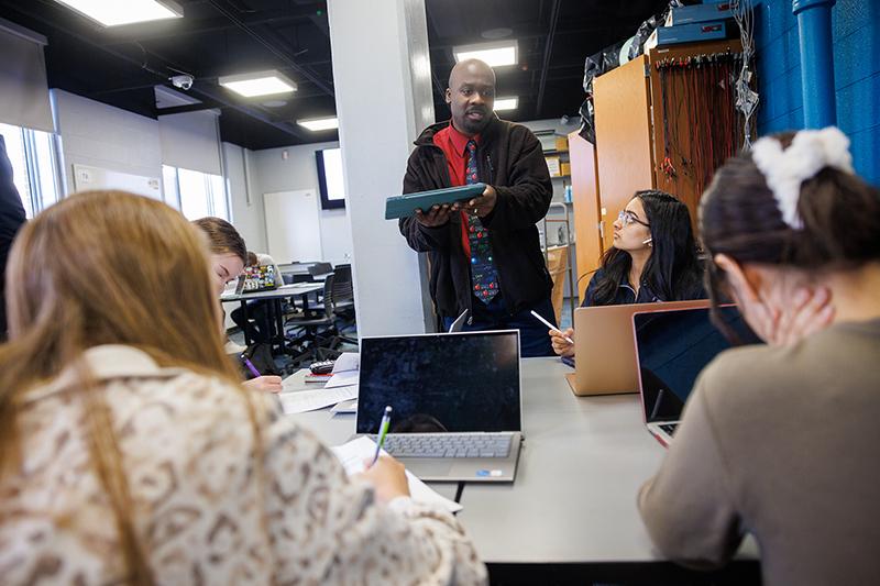 A physics faculty. member teaches concepts to a small group of students in a classroom