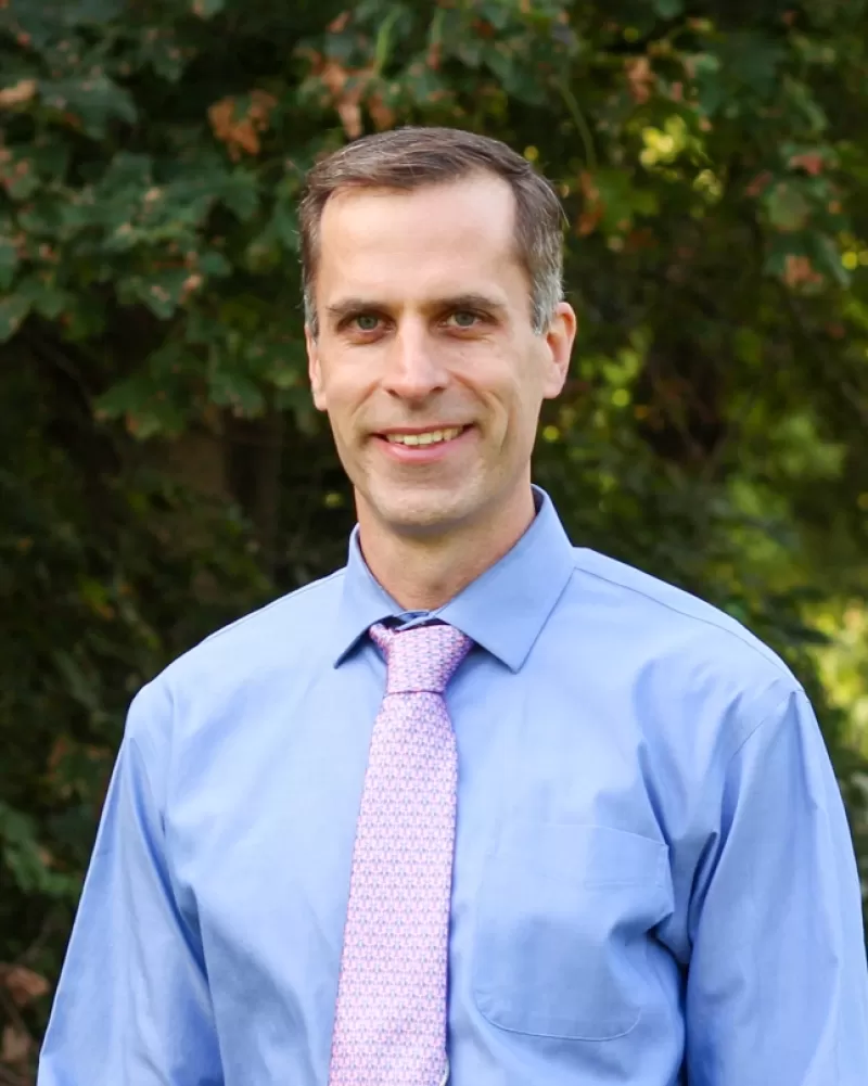 Ryan Sweeder wears a blue dress shirt and pale pink tie. He has dark hair