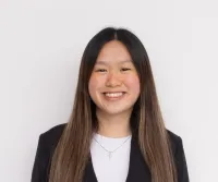 Tammy Thai has long brown hair and is smiling. She is wearing a black jacket, a white top, and a cross necklace